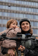 Woman wearing an Echo Pro Black headfirst helmet holding a child on a bicycle with a cityscape background