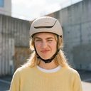 Person wearing a beige helmet with a brand logo, standing outdoors.