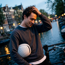 Man holding a white helmet by a canal with buildings and lights in the background. headfirst Echo Pro Beige Chris 7