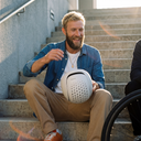 Man sitting on steps holding a white helmet, smiling outdoors.