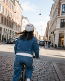 Person riding a bicycle on a city street wearing a helmet and denim outfit. headfirst_Echo_Pro_Beige_smart_brake_light_day