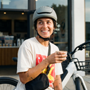 Person wearing a helmet and holding a coffee cup, standing next to a bicycle.