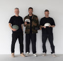 Three men standing side by side, each holding a helmet against a plain background