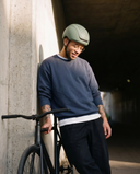 Man wearing a helmet and leaning against a wall with a bicycle.